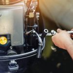 mechanic repairing inflatable motorboat engine at boat garage. Ship engine seasonal service and maintenance. Vessel motor with open cover.