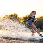 Female wakeboarder wakesurfing on sunset. Girl riding waterski cabel. Fron focus on water drops. Summer activities in the lake.