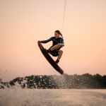 active strong man making trick in jump time with wakeboard on sky background. Summertime watersports activity